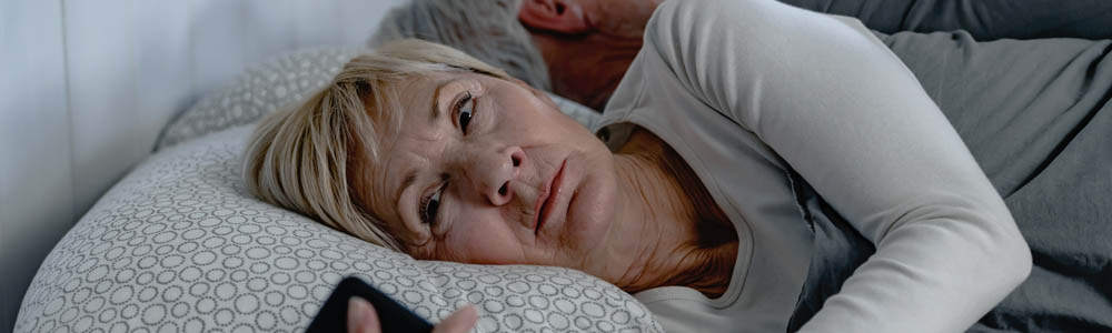Older woman lying awake, suffering from insomnia, holding her phone Older woman lying awake, suffering from insomnia, holding her phone